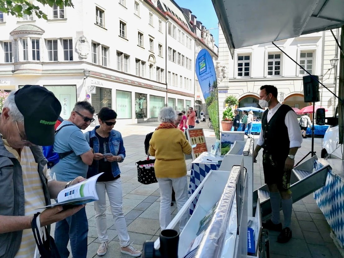 Vierter „Urlaubstruck“-Einsatz: Der Leiter des Tourismusbüros Prien Florian Tatzel (im Bild rechts) informierte gemeinsam mit dem Organisator der Werbefahrten Wolfgang Bude Interessenten über die Fülle an Sehenswürdigkeiten, Kulturschätzen und die einzigartige Naturlandschaft der Chiemsee Region. Für Stimmung am Regensburger Neupfarrplatz sorgte der Musiker Georg Dumberger mit bayerischer Volksmusik. Foto: Prien Marketing GmbH