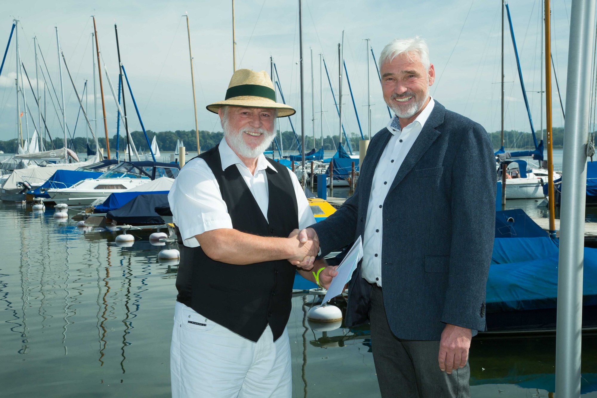 (v.l.n.r.) Dritter Bürgermeister Alfred Schelhas gratulierte dem Geschäftsführer der Chiemsee Marina GmbH Dirk Schröder zum 95.-jährigen Bestehen und überreichte einen Gutschein an die Crew des Sportboothafens Stippelwerft. Im Namen der Geschäftsführerin der Prien Marketing GmbH Andrea Hübner, überbrachte Schelhas je einen Gutschein für eine Veranstaltungen der PriMa.Bildrechte: Anita Berger